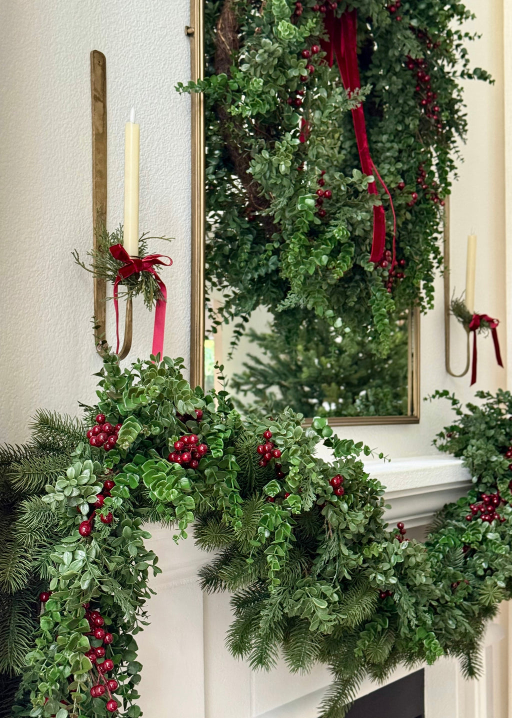 Decorative Christmas mantel with eucalyptus greenery, red berries, and a mirror.