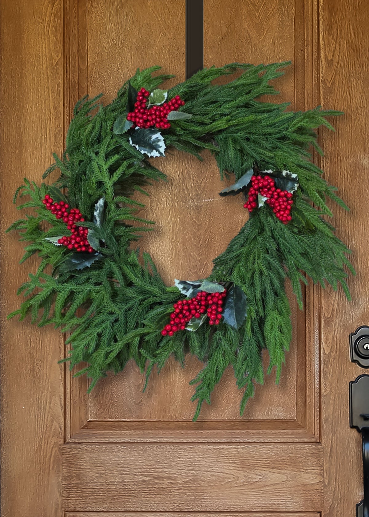 Artificial Holly and Red Berries Picks Decorating a Norfolk Pine Wreath on a Wood Door