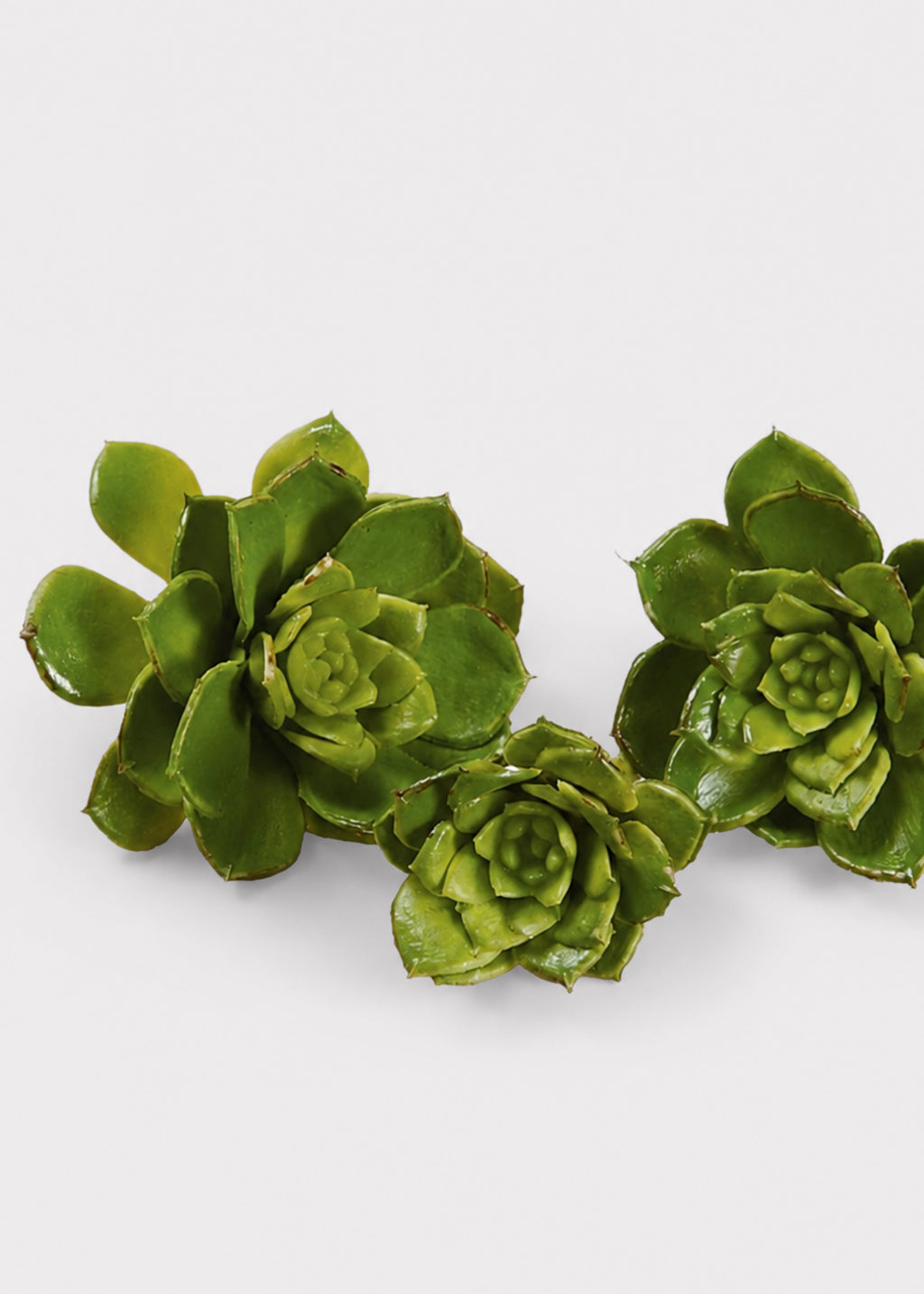 Three green artificial succulent plants with realistic rosette shapes, arranged on a plain light gray background.
