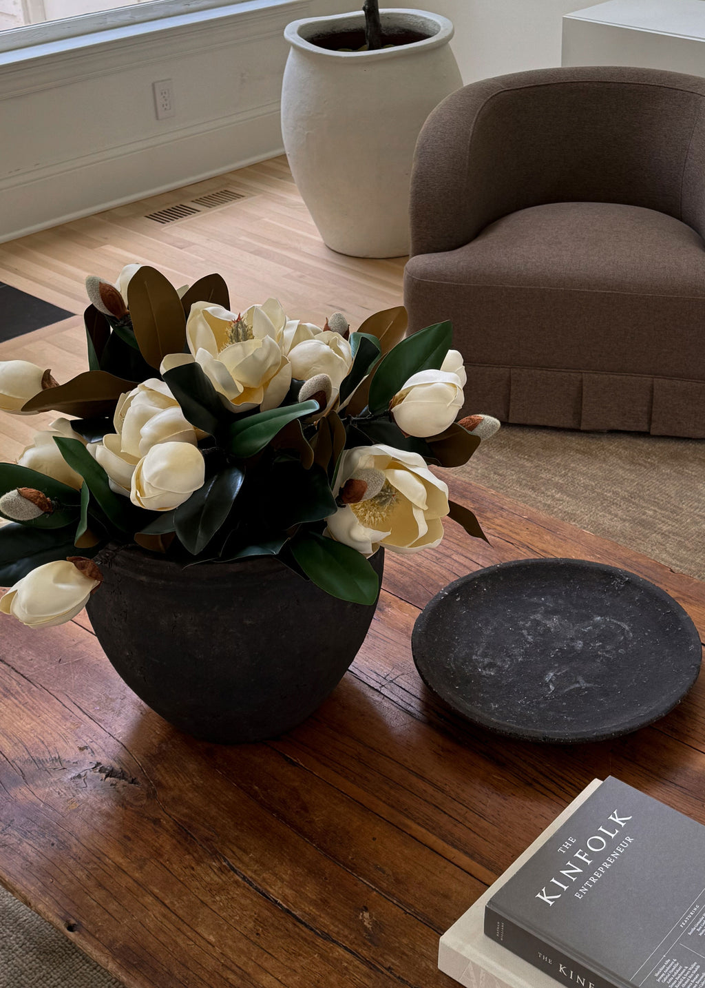 Faux magnolia arrangement in a pot on a coffee table. 