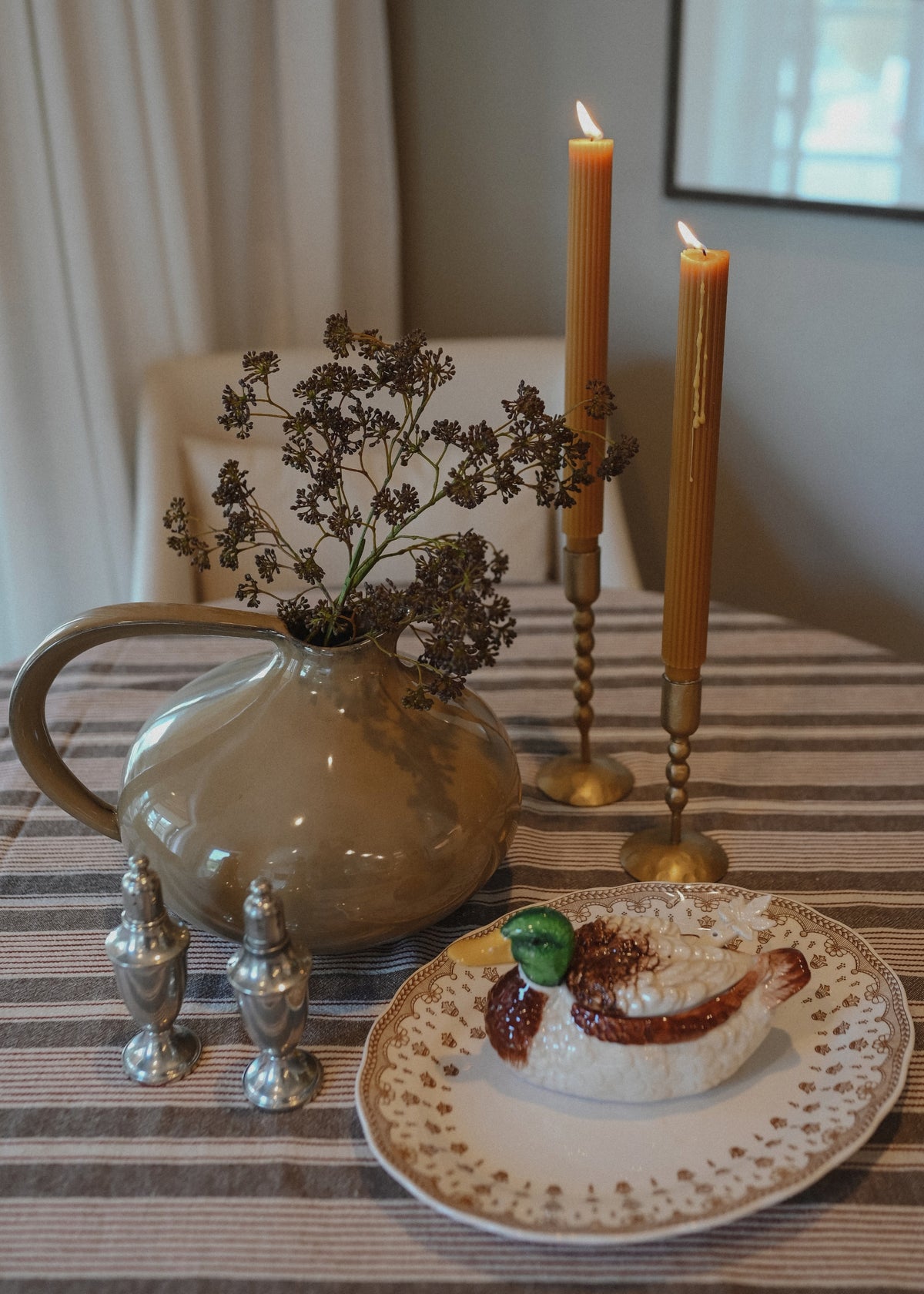 mauve sedum spray styled in a vase with taper candles decorating a table