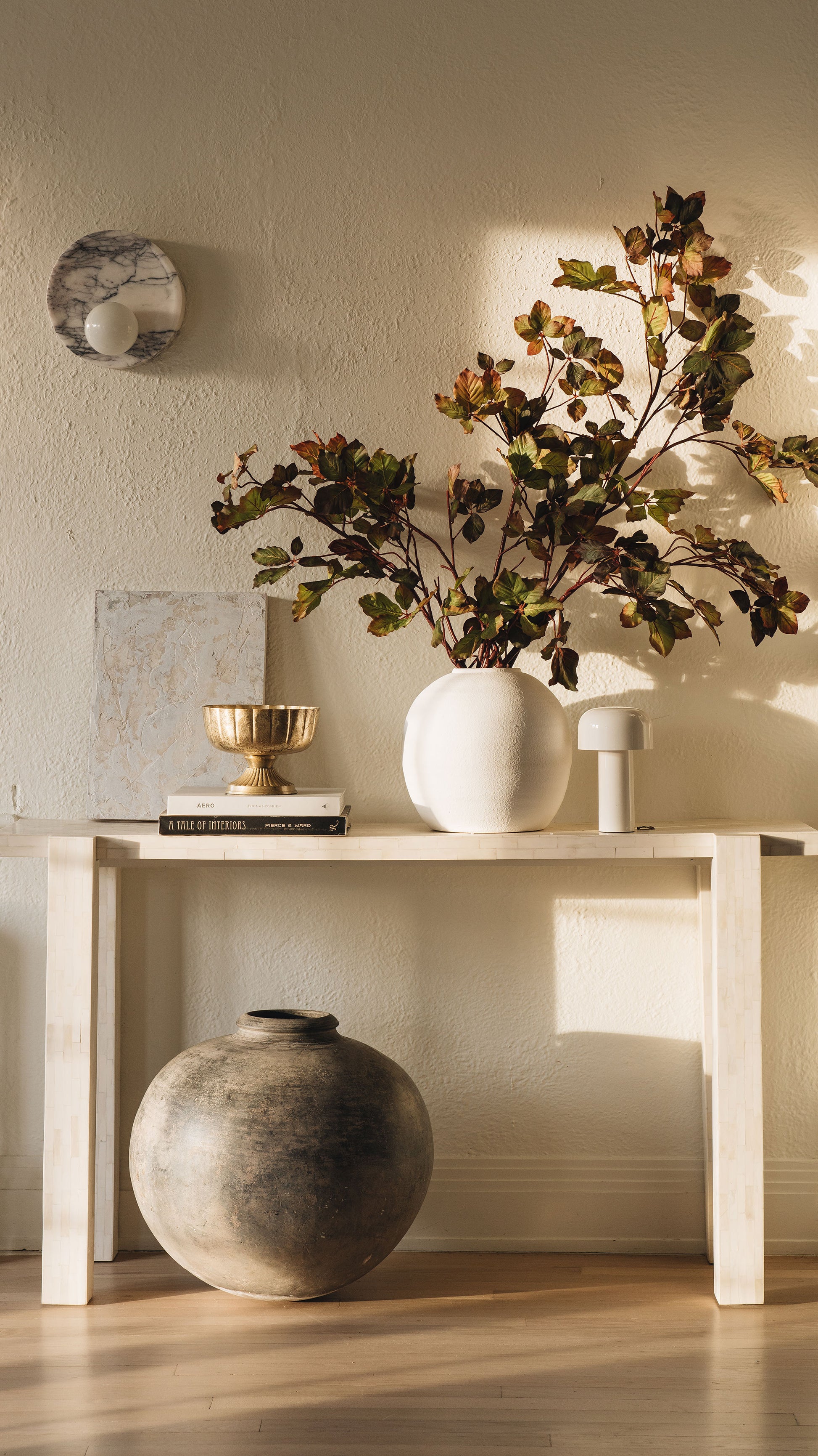 Decorative setup with a vase, books, and a plant on a table against a neutral wall.