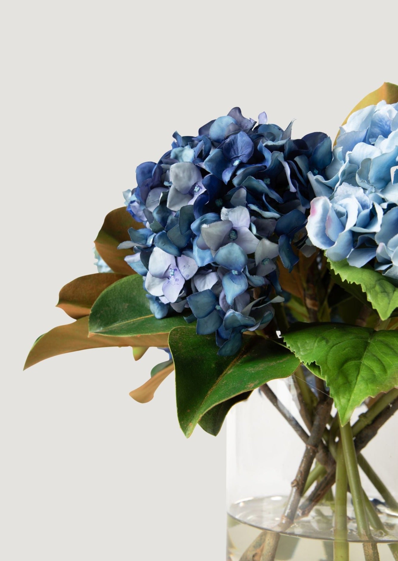 faux blue hydrangea and magnolia leaf arrangement in glass vase