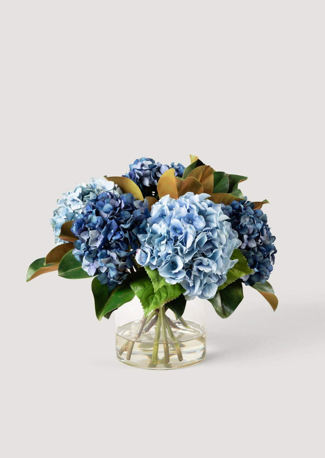 luxury faux flower arrangement of blooming blue hydrangeas in glass vase