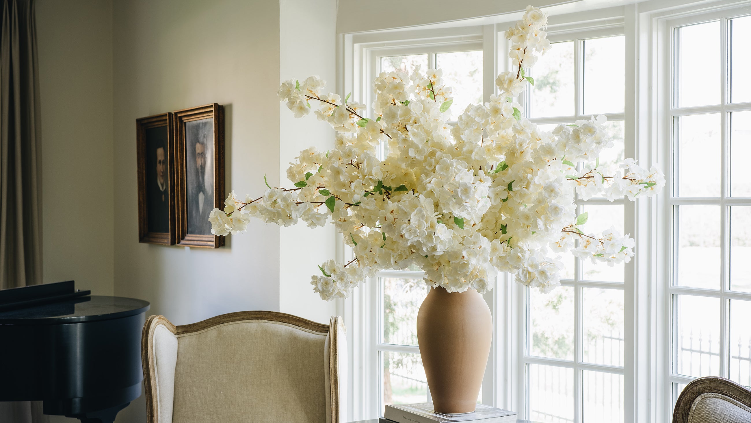 White flowers in a vase on a windowsill with a chair and piano in the background