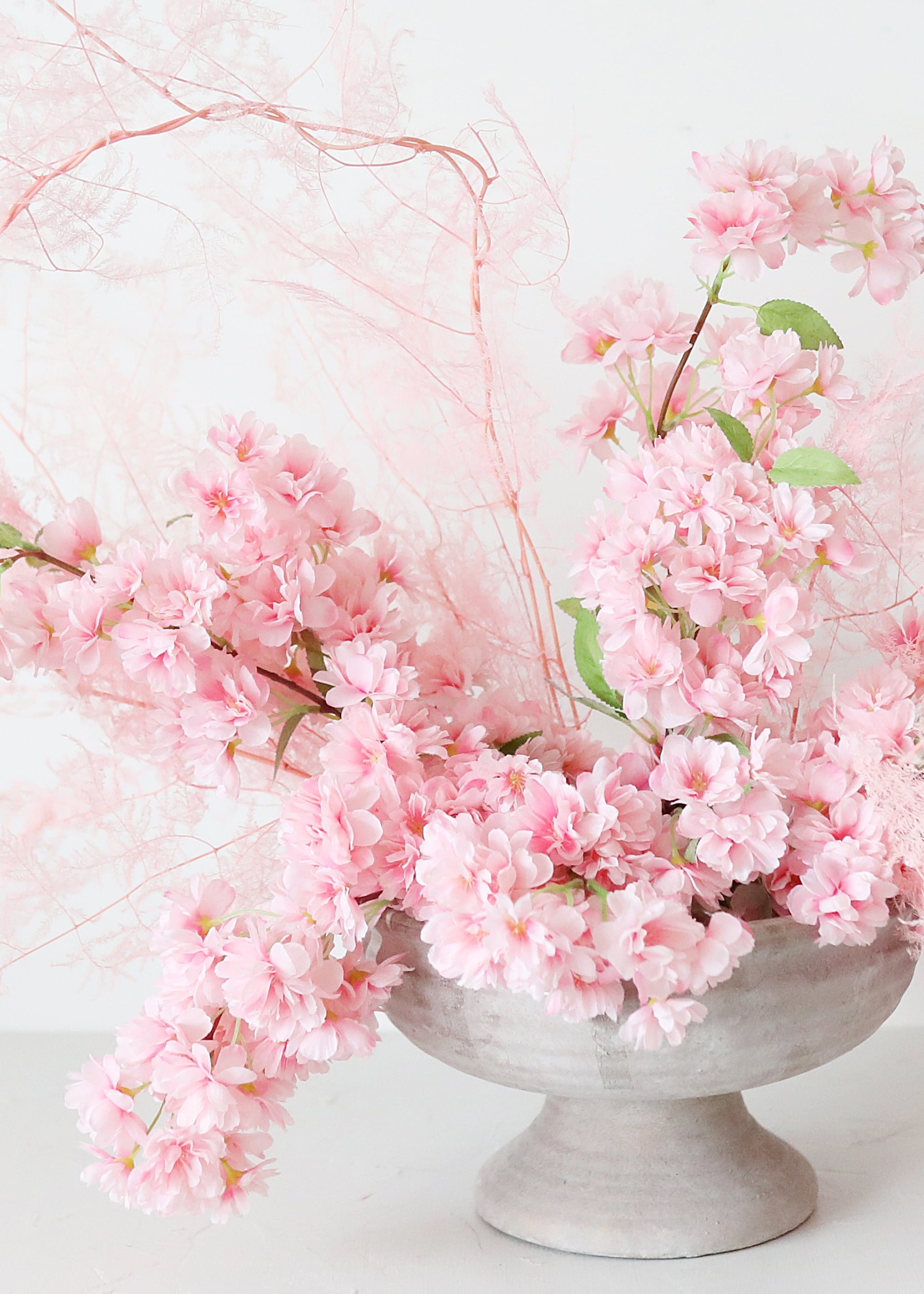 artificial pink cherry blossoms arranged in a pedestal vase