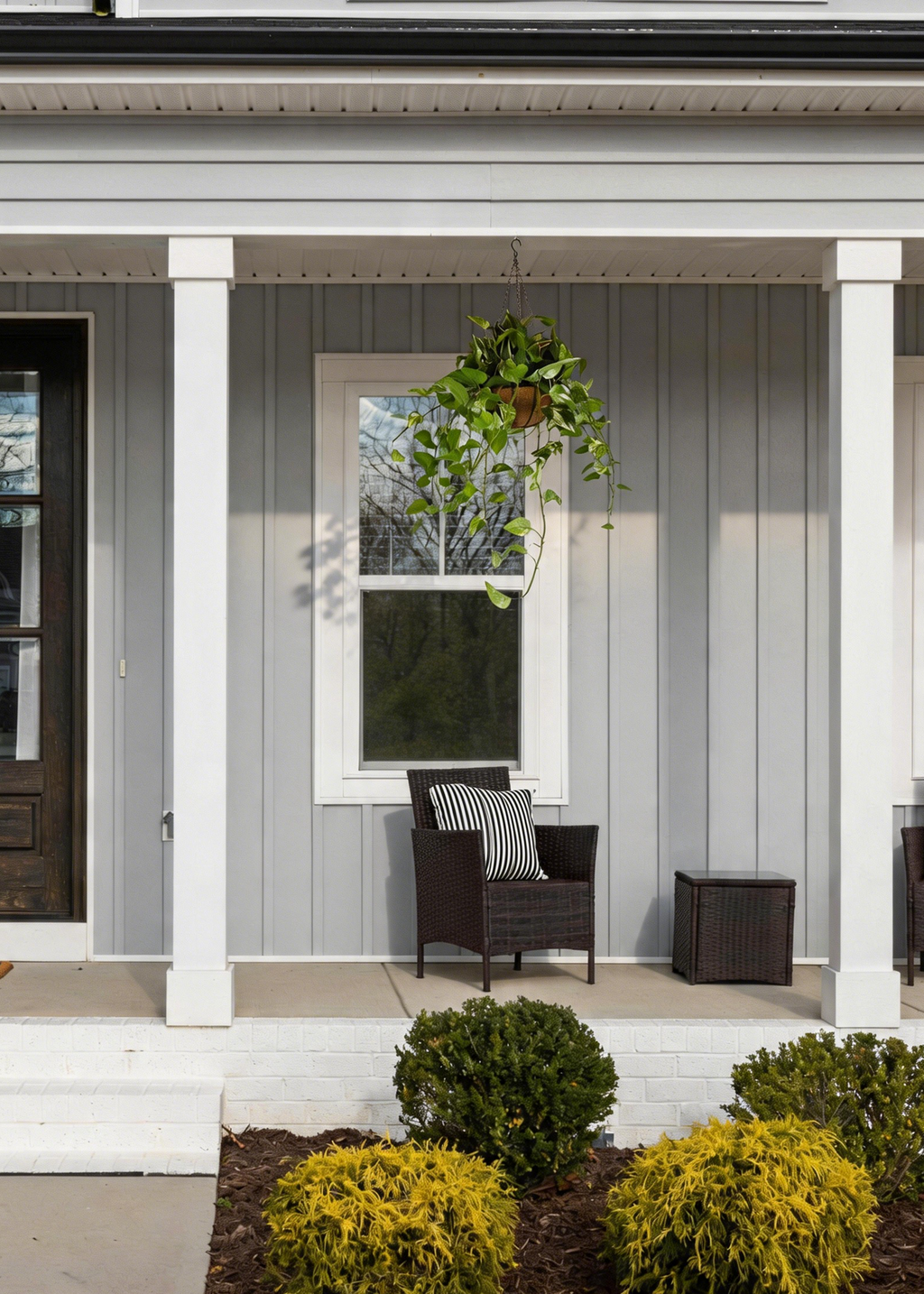 Front porch of a house with a chair, table, and decorative faux hanging plant