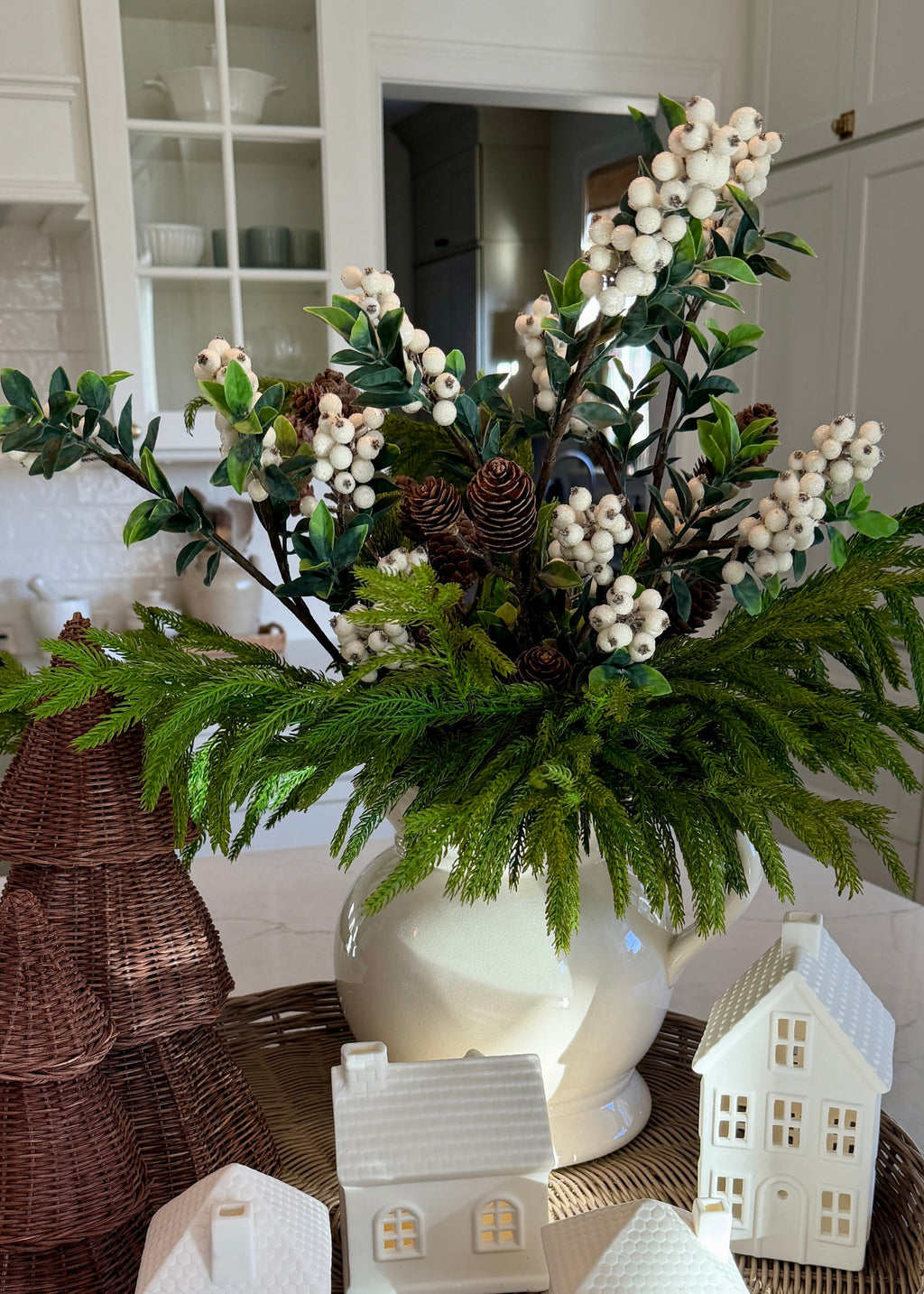 Decorative floral arrangement with greenery and white berries in a white vase on a table.