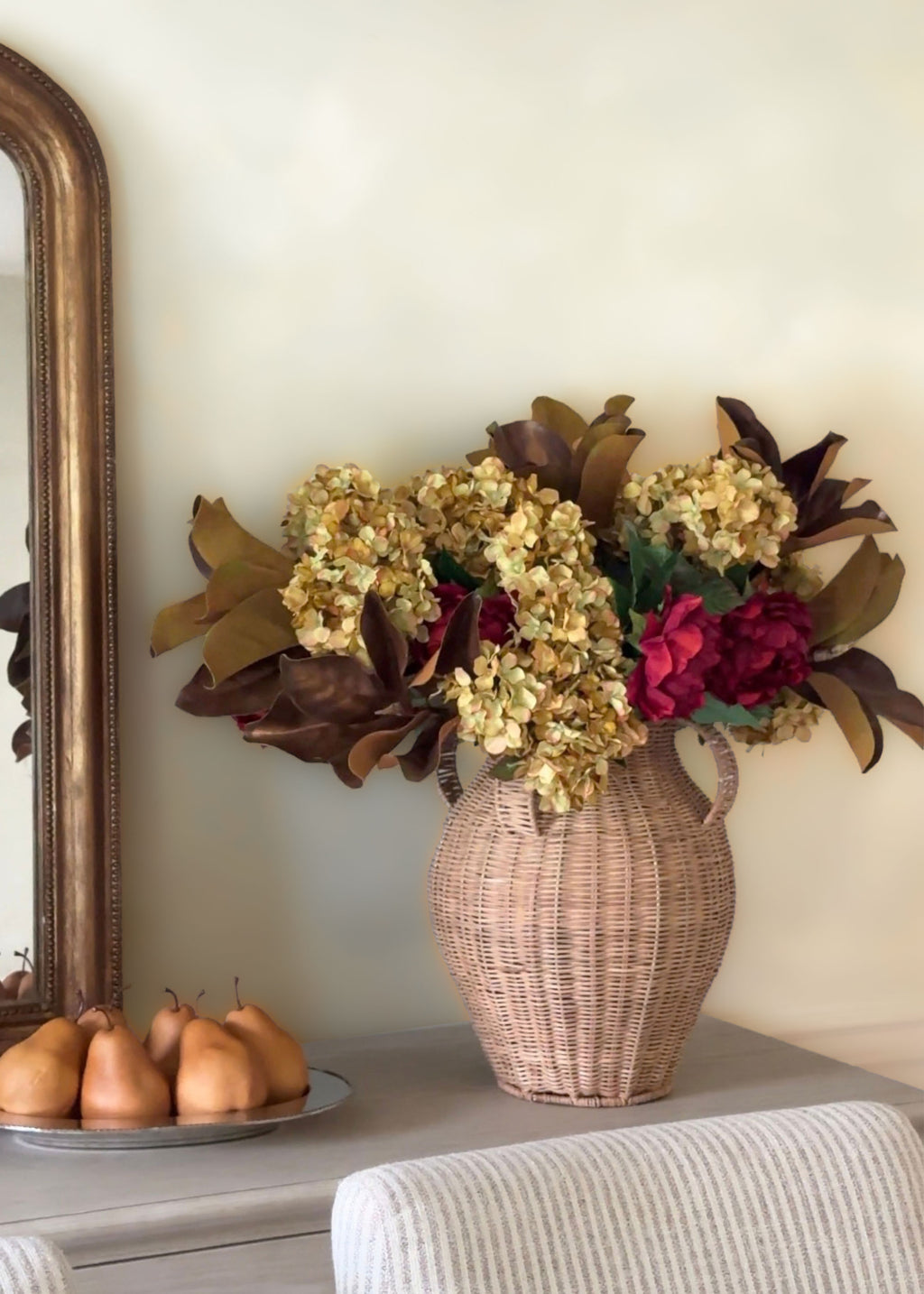 dried look faux hydrangeas, burgundy peonies, and fall magnolia leaves arranged in a wicker vase