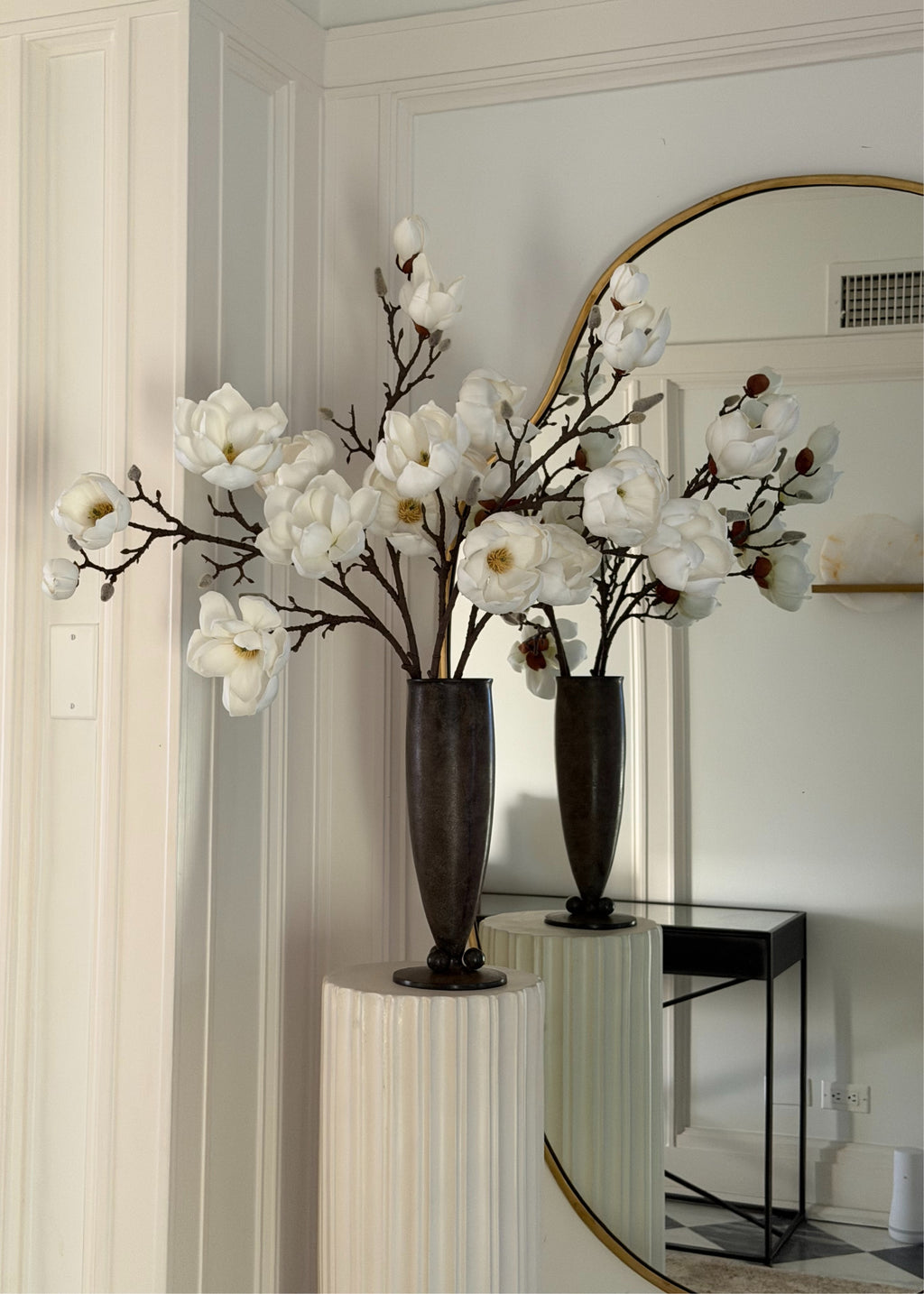 white faux magnolia flowers in black vase on a pedestal 