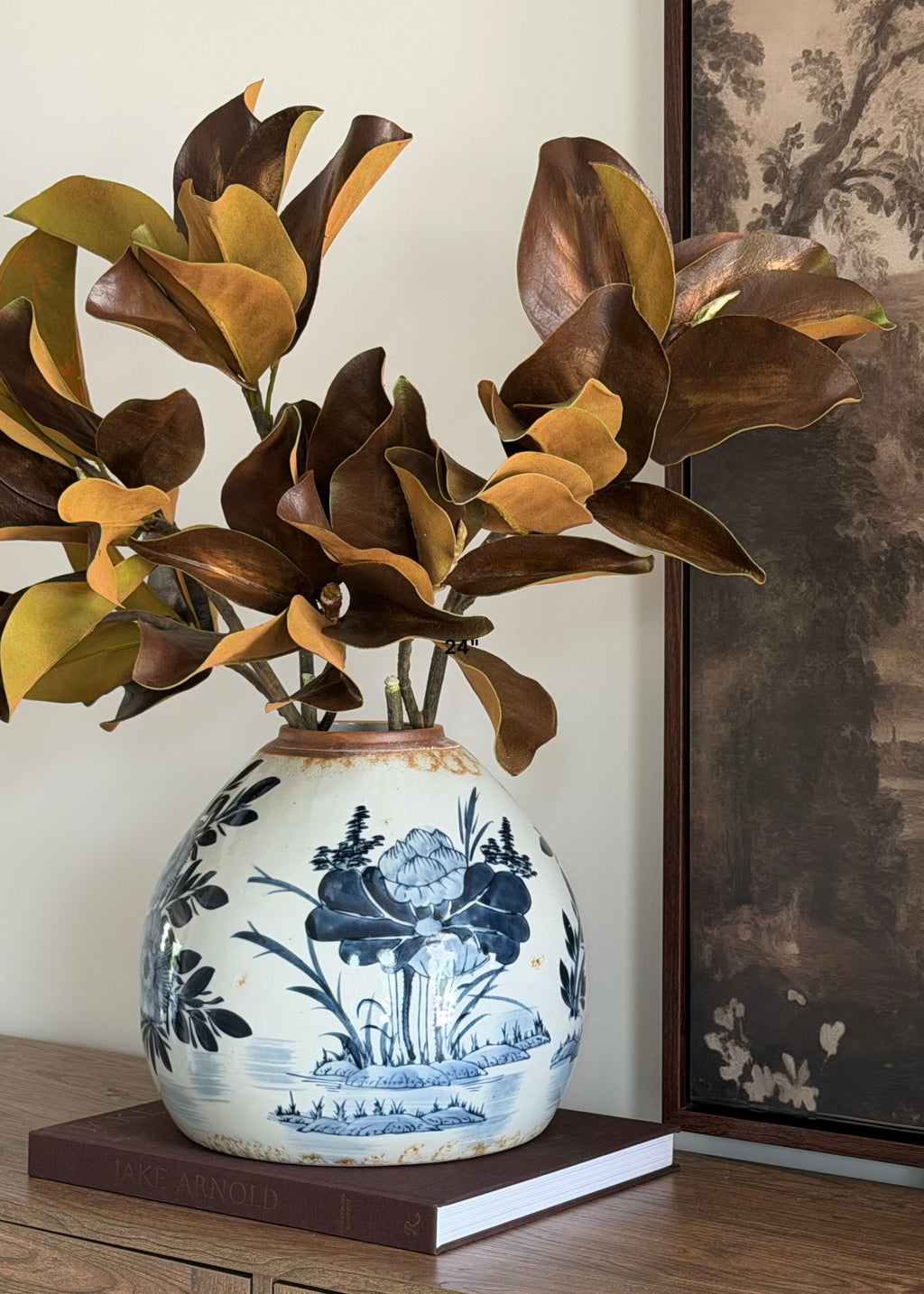 a video of arranging faux magnolia leaves in a blue and white ginger vase