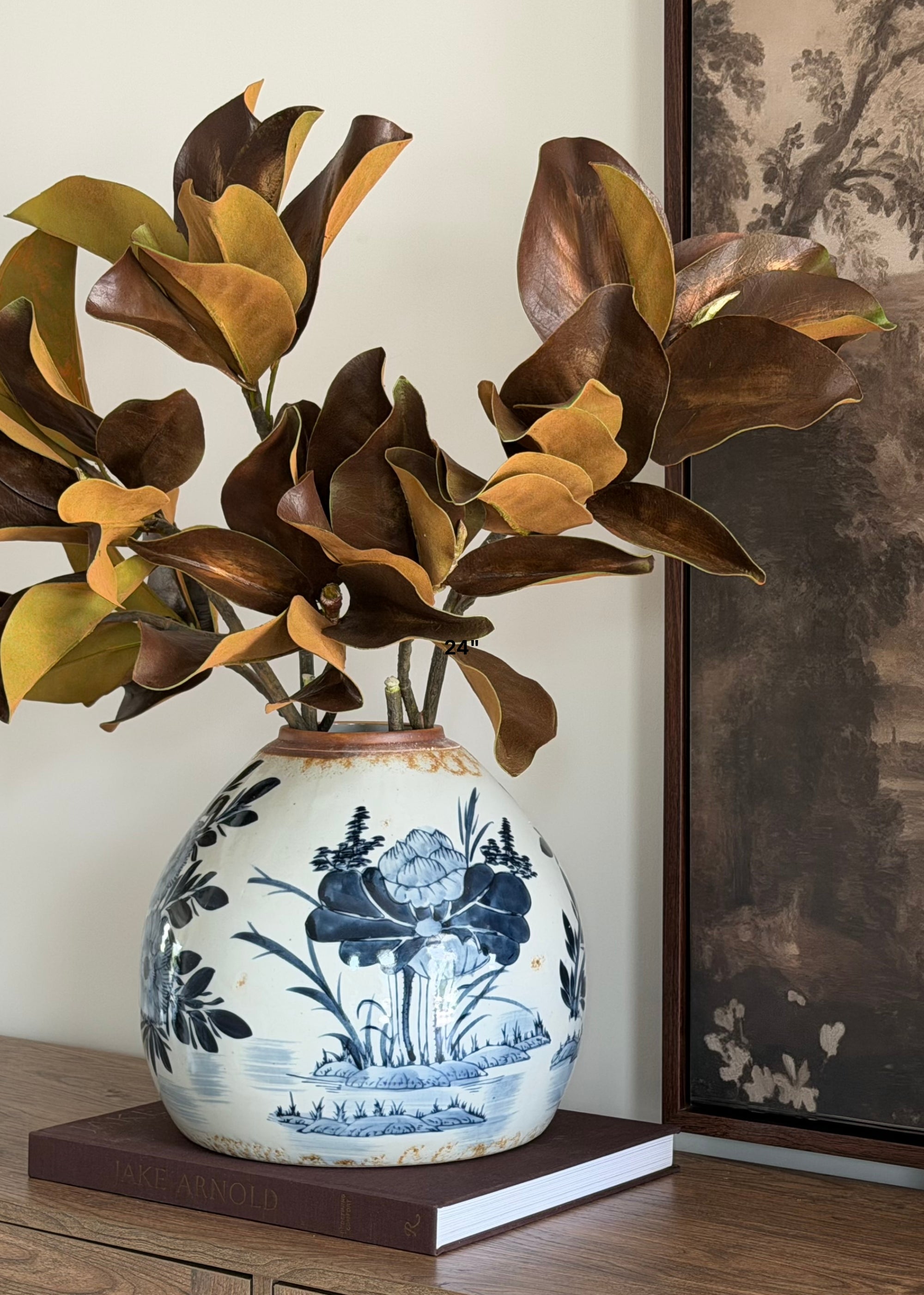 a video of arranging faux magnolia leaves in a blue and white ginger vase