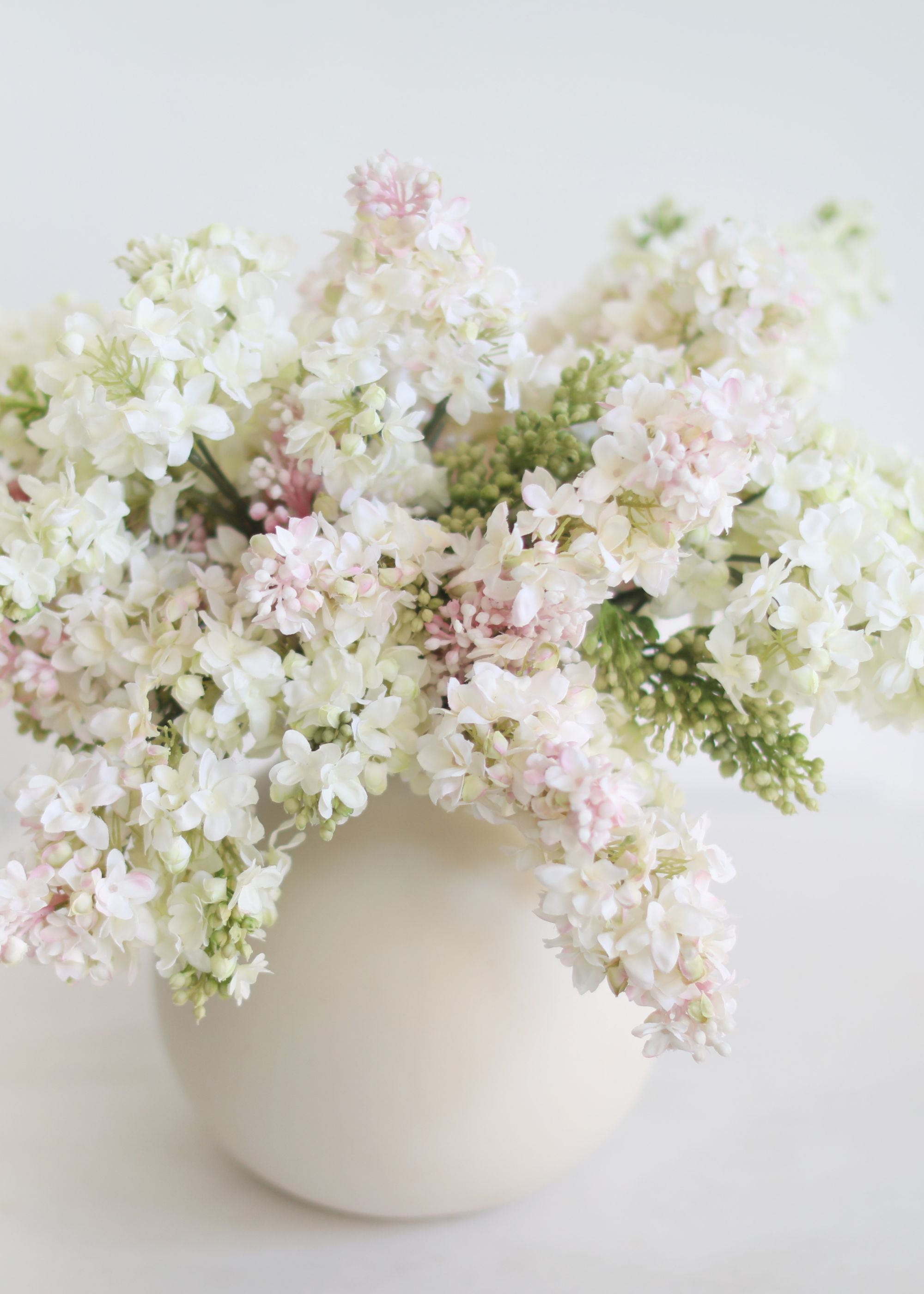 Arranging faux lilacs in a white vase