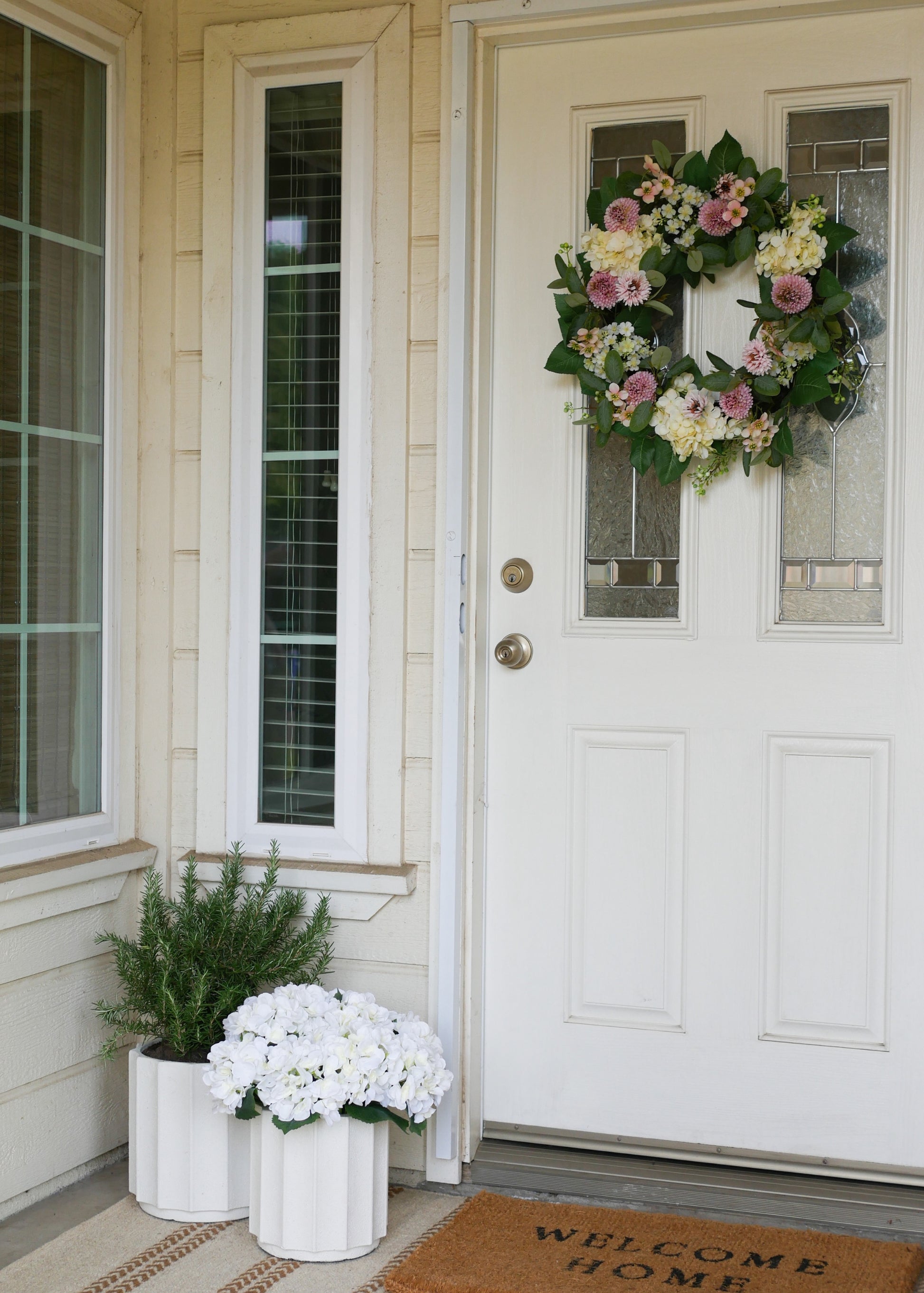 Front door with a floral wreath and potted plants