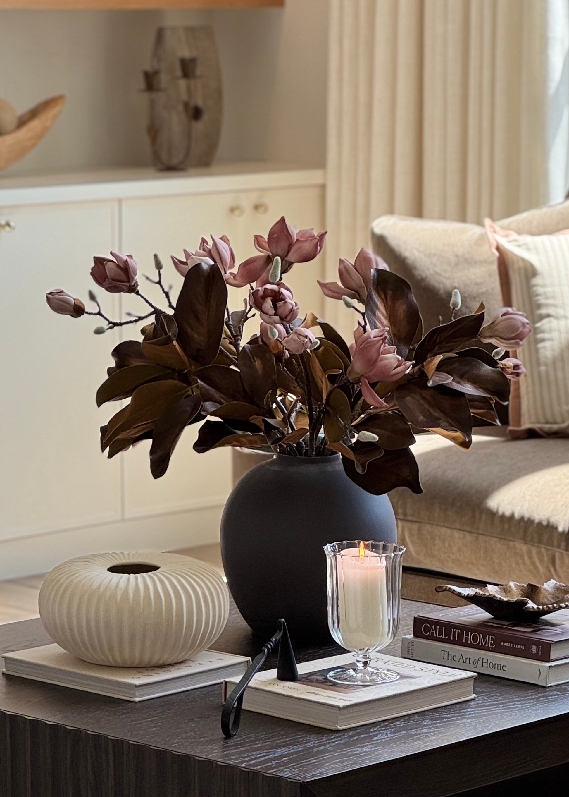video of arranging a faux mauve pink magnolia flower with warm brown magnolia leaves on a coffee table 