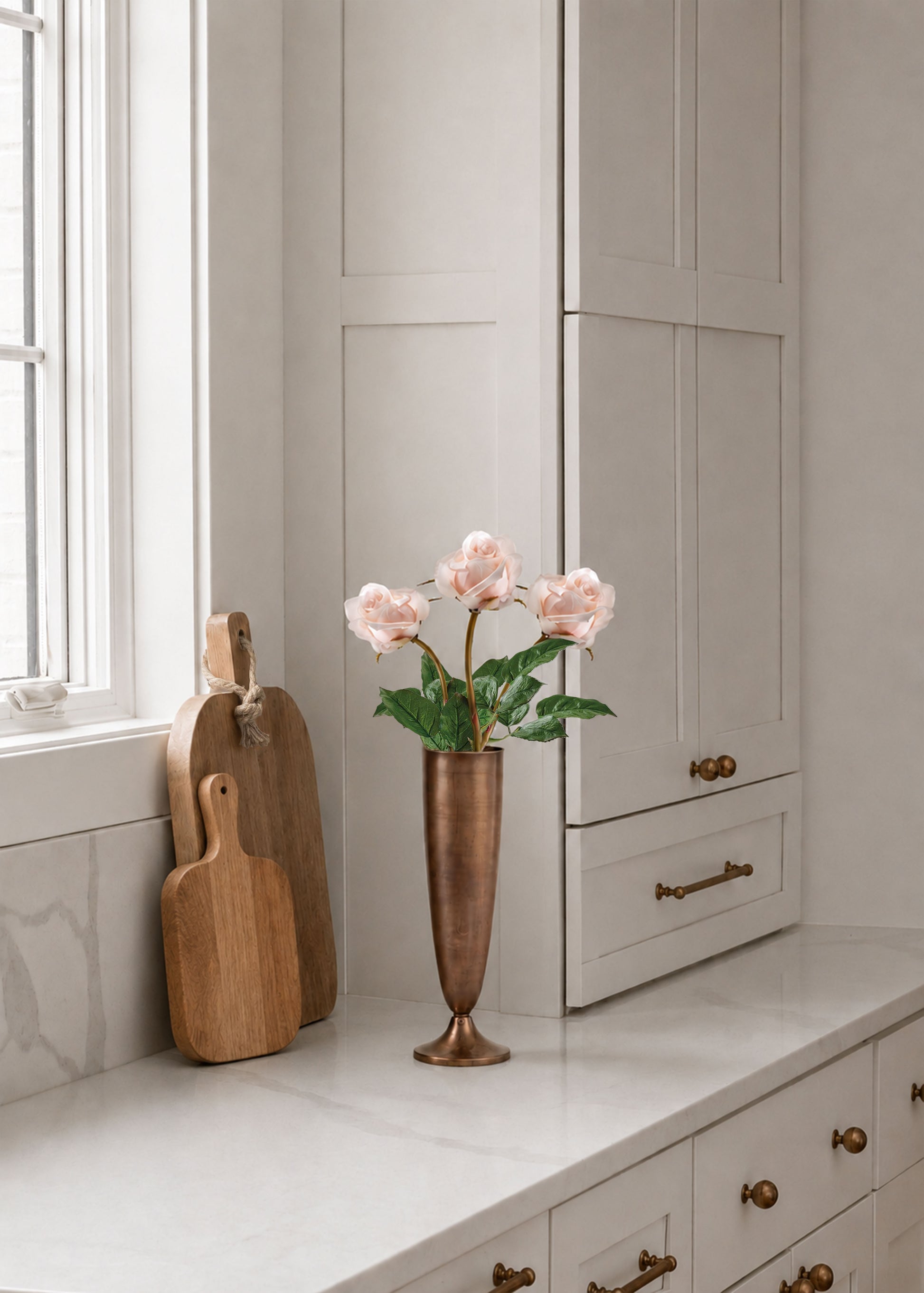 three rose buds arranged in a copper vase on a kitchen counter
