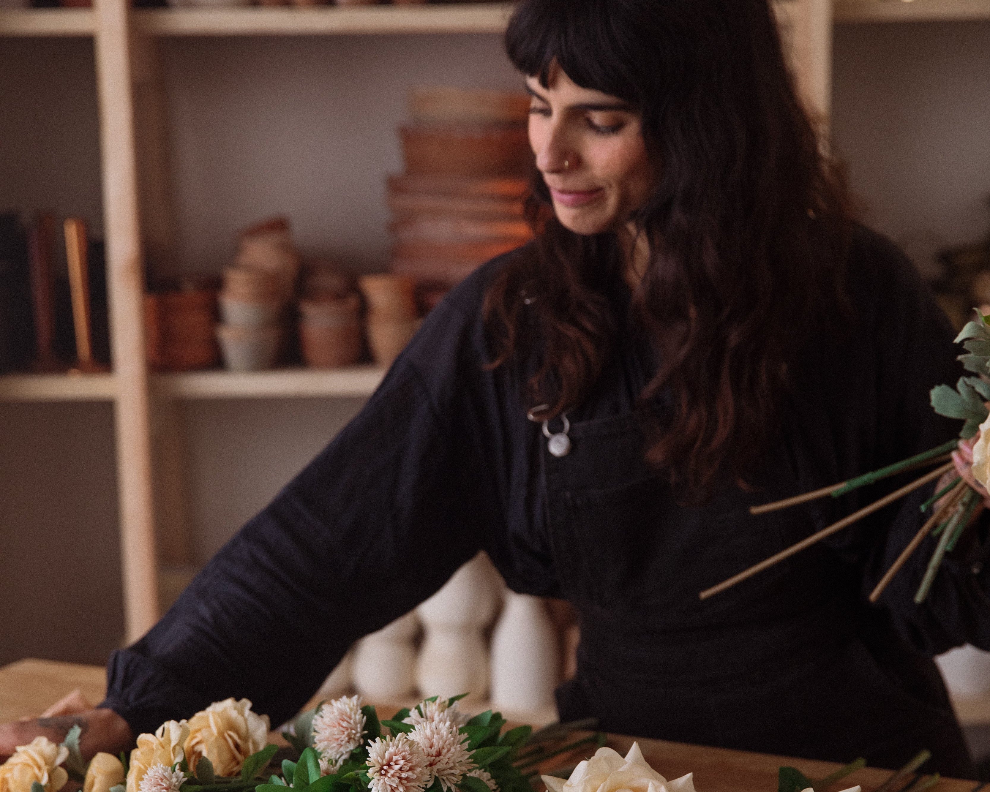 Rachael Ann Lunghi of Siren Floral Co arranging flowers in a workshop setting with shelves in the background