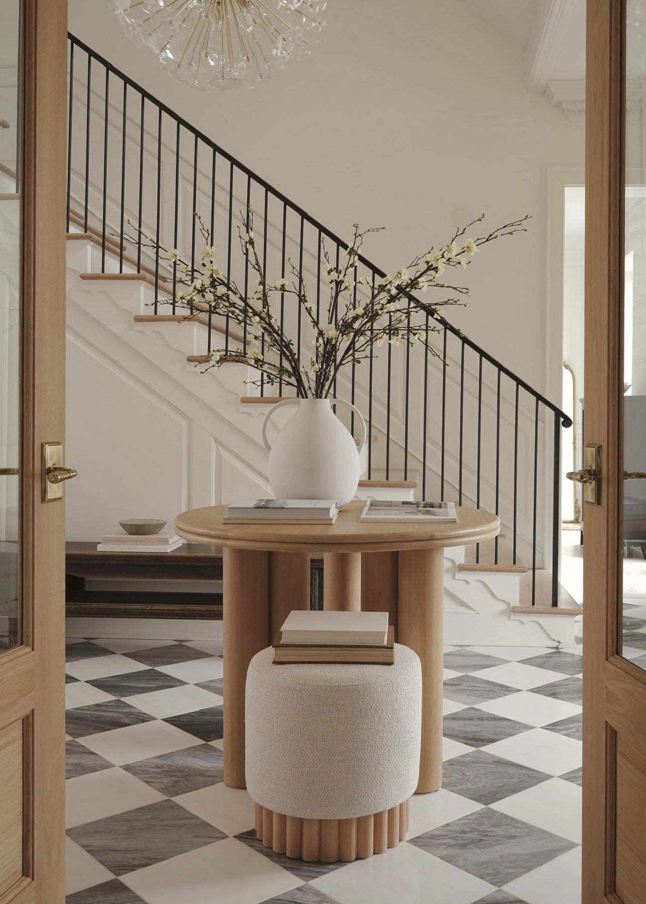 Foyer with a round wooden table, white vase with branches, and checkered floor.