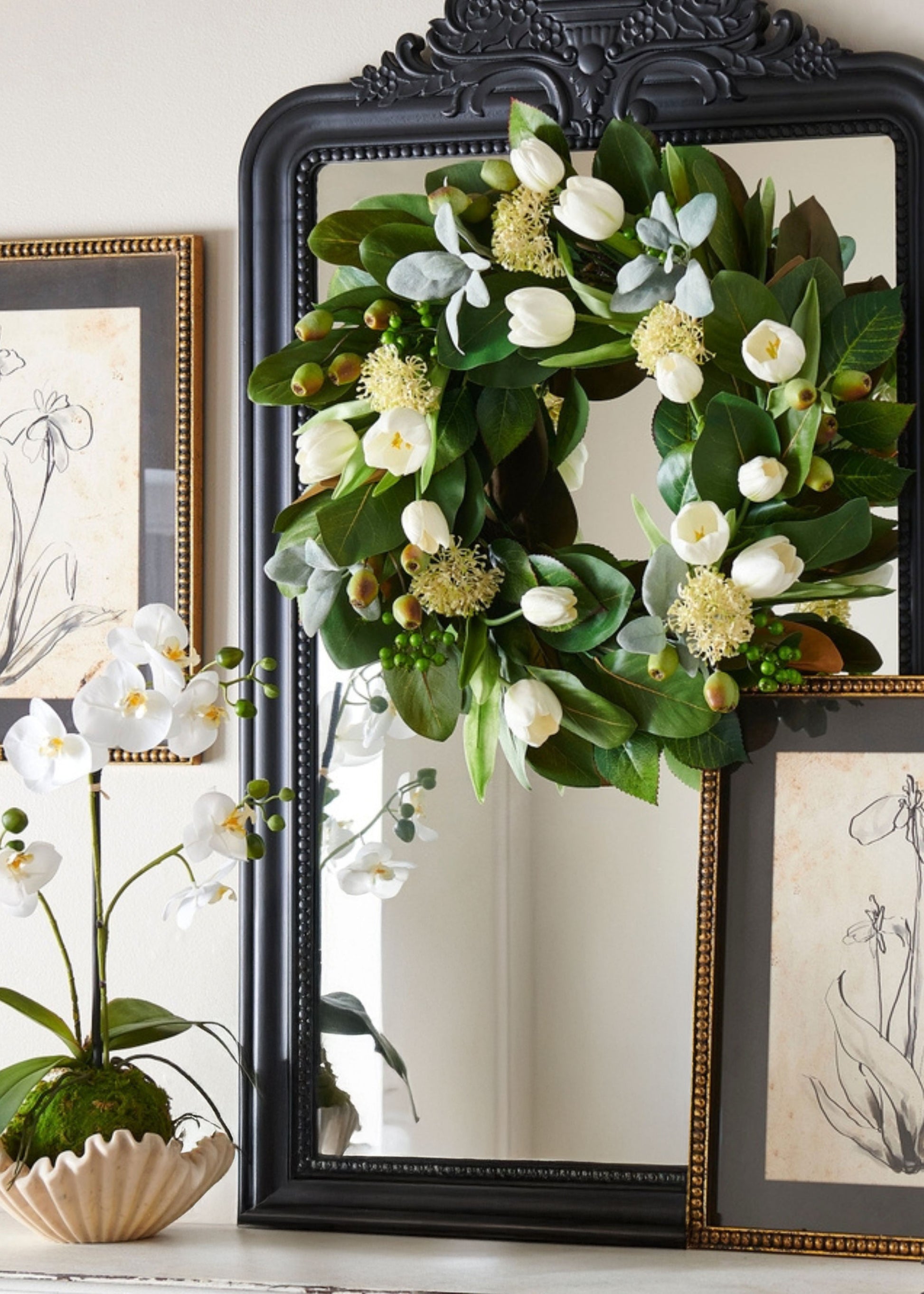 Floral wreath on a mirror with decorative frames and plants in the background